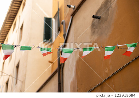 Typical street with houses in Italy. Facade of a yellow building with Italian flags. Italian flag in an old town narrow street of a city in Italy Typical street with houses in Italy. Facade of a yellow building with Italian flags. Italian flag in an old town narrow street of a city in Italy 122919094