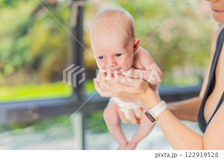 A mother gently soothes her newborn by holding them under the chest and bottom, offering comfort and security. A nurturing moment of calm and reassurance, symbolizing the tender care and bond between 122919528