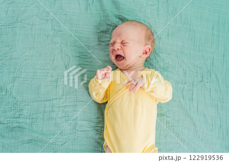 A newborn baby cries while lying on a soft muslin swaddle, expressing emotions and seeking comfort. A tender and natural moment of early infancy, symbolizing vulnerability, needs, and parental care 122919536