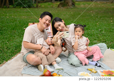Cheerful family taking a selfie with mobile phone during their outdoor picnic 122920206