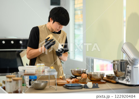 Young baker wearing gloves preparing ingredients for cookie dough Young baker wearing gloves preparing ingredients for cookie dough 122920484