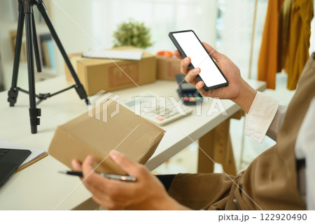 Close up of an entrepreneur checking orders on smartphone at a workspace filled with shipping boxes Close up of an entrepreneur checking orders on smartphone at a workspace filled with shipping boxes 122920490