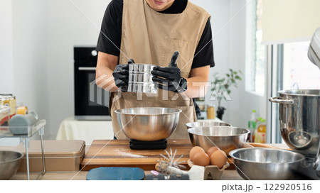 Male baker sifting flour for chocolate chip cookies dough over kitchen counter 122920516
