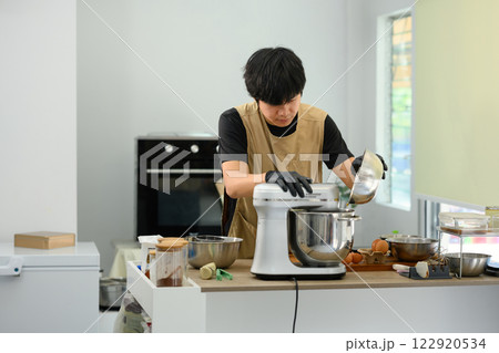 Man wearing black gloves pouring flour into stand mixer while preparing cookie dough 122920534
