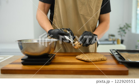 Baker wearing black gloves scooping chocolate chip cookie dough onto a baking tray Baker wearing black gloves scooping chocolate chip cookie dough onto a baking tray 122920551