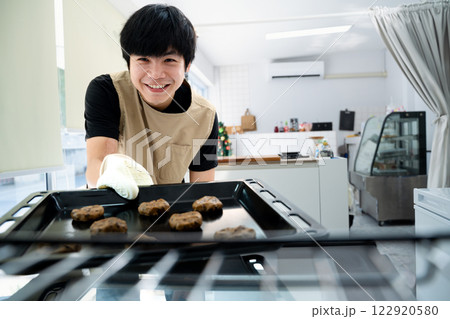 Cheerful small business owner putting a tray of chocolate chip cookies into the oven Cheerful small business owner putting a tray of chocolate chip cookies into the oven 122920580