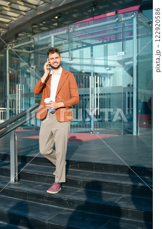 Stylish businessman having phone conversation while walking out of office building 122920586