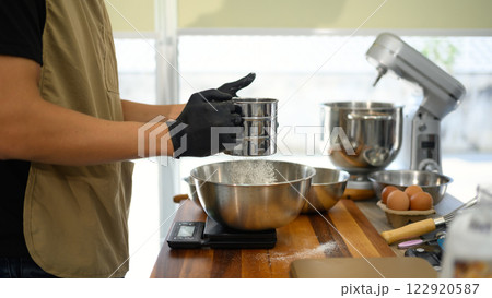 Baker sifting flour while preparing ingredients for cookie dough 122920587
