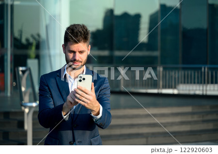 Professional businessman in a suit checking smartphone outside a contemporary office building Professional businessman in a suit checking smartphone outside a contemporary office building 122920603
