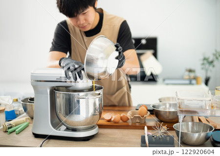 Male baker adding ingredients to a stand mixer for cookie dough 122920604