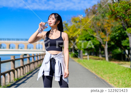 川沿いの道を歩きながら水分補給するかっこいい女性　エクササイズ　有酸素運動　トリミングアップ 122921423