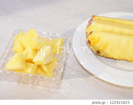 Piece of pineapple in glass bowl on white wood background. 122921625