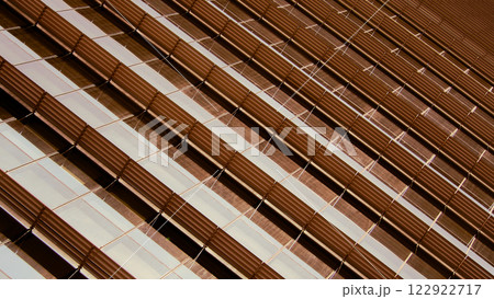 Detailed view of a building facade with a dynamic pattern of diagonal, ribbed metallic panels and reflective glass, creating a sense of depth and texture. 122922717