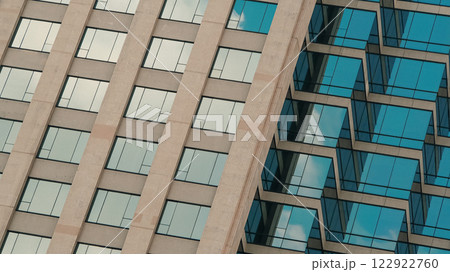 A striking architectural composition showcasing a grid of windows reflecting the sky, with alternating patterns that create a dynamic sense of depth and rhythm. 122922760