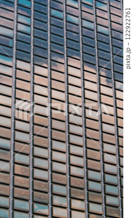 A close-up of a modern building facade featuring a grid of reflective rectangular windows, with soft reflections of the sky adding an artistic touch. 122922761