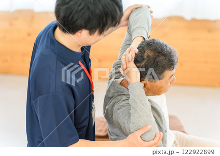 リハビリで体操をするシニア男性と理学療法士・作業療法士の男性スタッフ 122922899