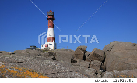 Blue sky over the red and white cast iron Eigeroy Lighthouse and anorthosite rock formations, Norway. 122925396