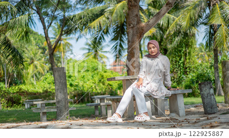 Woman in Hijab Relaxing on a Bench Under Palm Trees at a Tropical Beach Resort 122925887