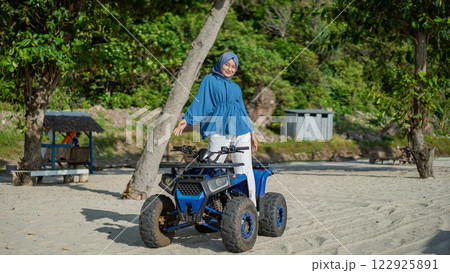 Stylish Muslim Woman Posing with Blue ATV on Tropical Beach Sand Adventure 122925891