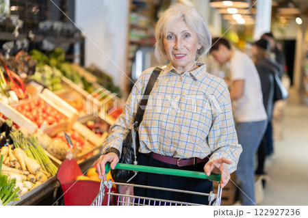 Elderly woman with shopping cart chooses groceries 122927236