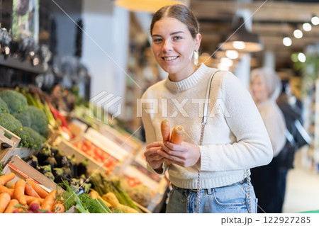 In cozy self-service store, young woman customer takes carrot out of box In cozy self-service store, young woman customer takes carrot out of box 122927285