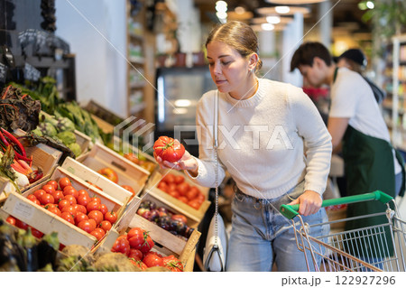 In cozy self-service store, girl customer takes tomatoes out of box In cozy self-service store, girl customer takes tomatoes out of box 122927296