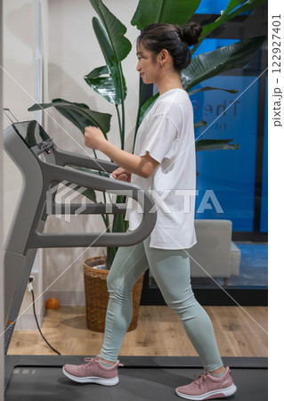 室内のジムのランニングマシンでランニングをする若い女性 室内のジムのランニングマシンでランニングをする若い女性 122927401