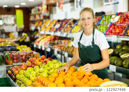 Hardworking girl who works part-time as a trainee saleswoman puts oranges Hardworking girl who works part-time as a trainee saleswoman puts oranges 122927496
