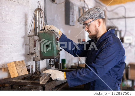 Young man drilling holes in metal part Young man drilling holes in metal part 122927503