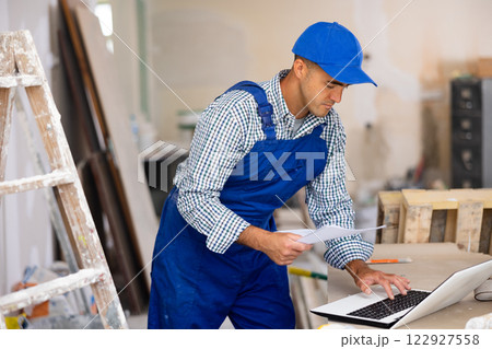 Man builder checking project documentation and using laptop Man builder checking project documentation and using laptop 122927558