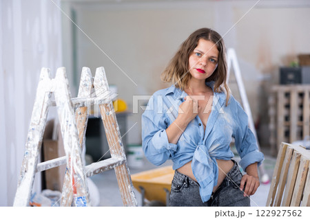 Attractive young woman in denim shirt and shorts posing next to stepladder in refurbished room 122927562