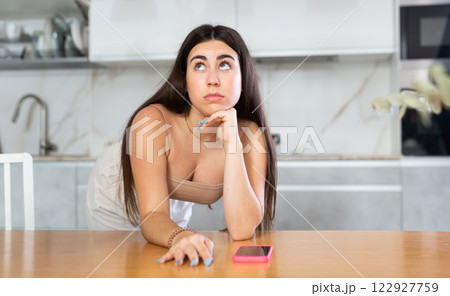 Young woman waiting for message on phone in kitchen Young woman waiting for message on phone in kitchen 122927759