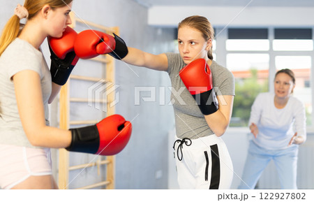 Teenage girl in boxing gloves practicing punches in sparring at self defense training Teenage girl in boxing gloves practicing punches in sparring at self defense training 122927802