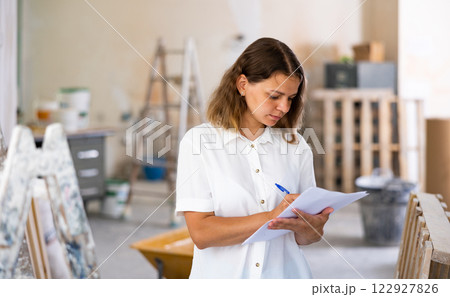 Woman with documents in her hands checks the quality of the completed repairs in cottage room Woman with documents in her hands checks the quality of the completed repairs in cottage room 122927826