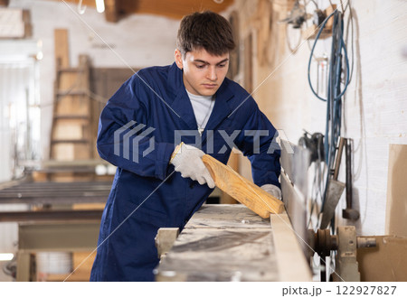 Young guy working with wooden board on workbench 122927827