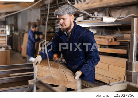 Male worker carries board from storage location to processing location. Selects planks for furniture manufacture 122927856