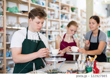 Young woman teaching teen boy and teen girl how to make ceramic cup 122927865