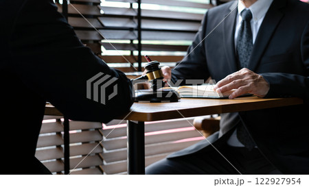 Two legal professionals in formal attire discussing case with gavel on desk, justice, law consultation, and corporate legal decisions Two legal professionals in formal attire discussing case with gavel on desk, justice, law consultation, and corporate legal decisions 122927954