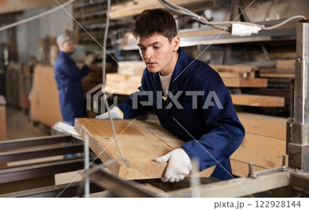 Young guy putting wooden board on cutting machine Young guy putting wooden board on cutting machine 122928144