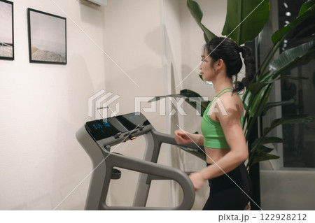 ジムでトレーニングウェアを着てランニングマシンで走る若い女性 ジムでトレーニングウェアを着てランニングマシンで走る若い女性 122928212