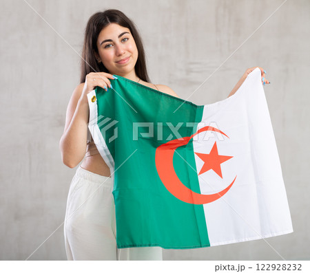 Happy young woman with flag of Algeria against unicoloured background 122928232