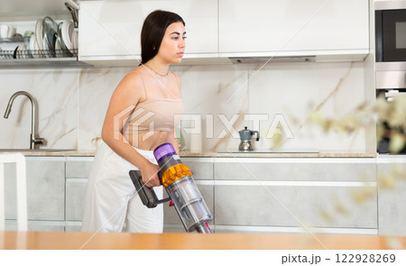 Positive young woman vacuum-cleaning the floor in the kitchen Positive young woman vacuum-cleaning the floor in the kitchen 122928269