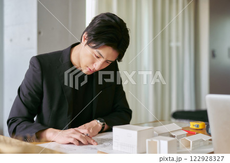 建物の図面と模型を見て建築の研究をする大学の工学部の建築学科に務める男性の教授 122928327
