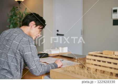 建築事務所で建築も模型を横に置いて建物の設計図を書く設計士の1人の男性 122928330
