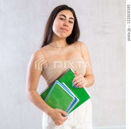 Young woman posing with notebooks against wall 122928395