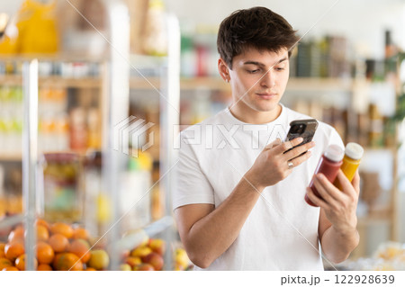 Female shopper scans QR code on bottle of smoothie with her smartphone Female shopper scans QR code on bottle of smoothie with her smartphone 122928639