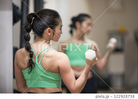 トレーニングウェアを着てダンベルで筋トレをしている若い女性 122928738