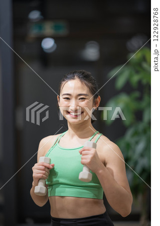 トレーニングウェアを着てダンベルで筋トレをしている若い女性 122928768