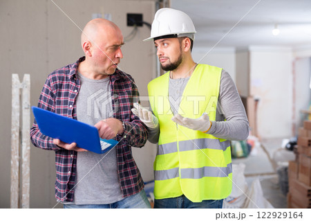 Puzzled builder talking with displeased man with laptop in home during renovation 122929164