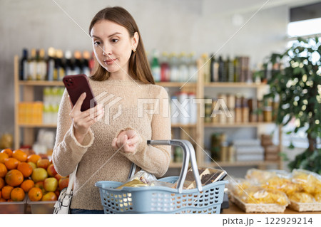 Visiting store, girl scrolling phone screen and looking for something in showcase. 122929214